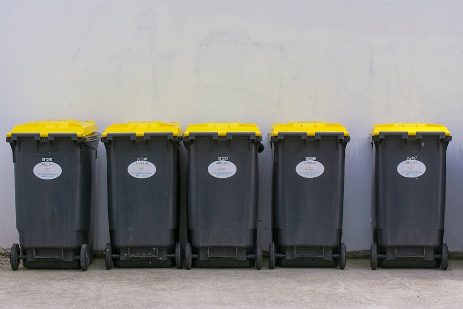 A black wheeled rubbish bin positioned on a sidewalk at night, with a mixture of plastic and paper waste visible overflowing from the open lid. The bin features a white label with the text 'St. John's